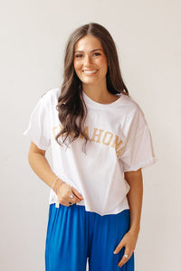 Woman wearing a white t-shirt with text  saying oklahoma and blue pants against a white background