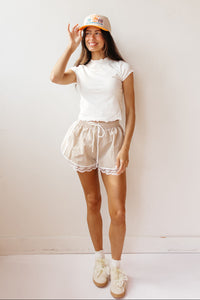 Woman wearing a white t-shirt, beige athletic shorts with lace trim and a OKC thunder cap against a plain background