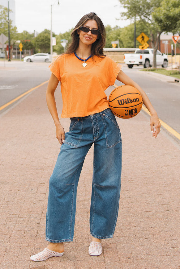 mode model Taylor wearing barrel jeans and orange tee shirt holding a basketball on a street with 'Thunder Up' sign in the background